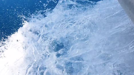 the bow of a metal motorboat moving through the deep blue ocean water with whitewash wake and sea spray