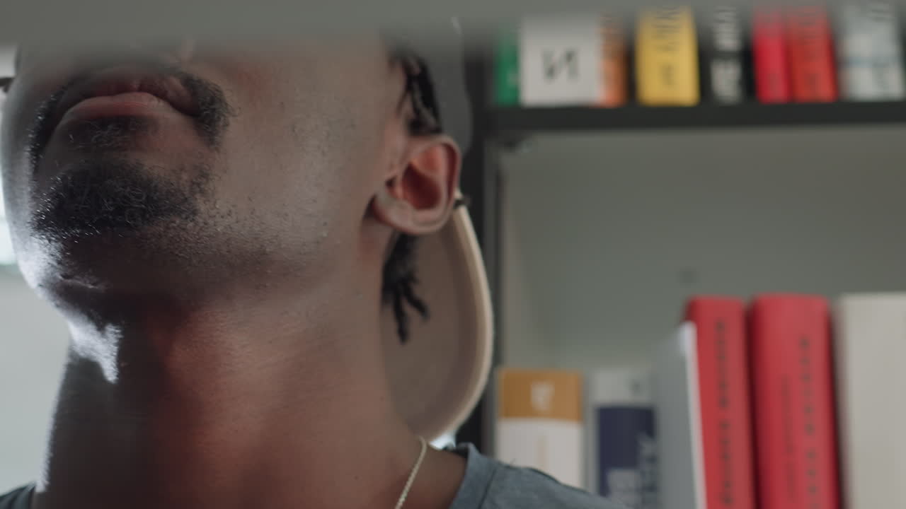Close up of focused student wearing cap reaching toward shelf to take book, face partially hidden by book edge, soft background blur showing rows of books in library setting