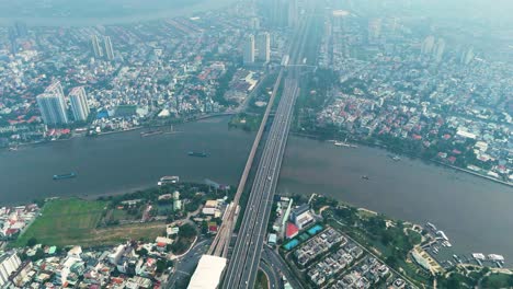 aerial: saigon bridge during the day with fog, traffic, cityscape, and the saigon river in ho chi minh city, vietnam, establishing drone shot