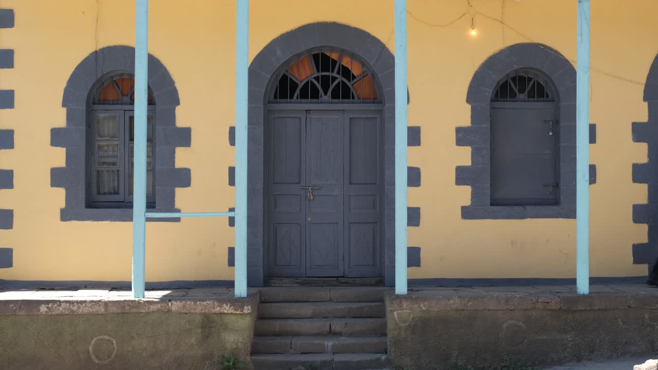 Man in casual clothes, walking quickly past a traditional building with arched windows, a closed door and blue pillars, slow motion shot