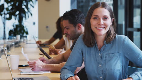 Portrait-Of-Businesswoman-Working-At-Desk-On-Laptop-In-Shared-Open-Plan-Office-Workspace