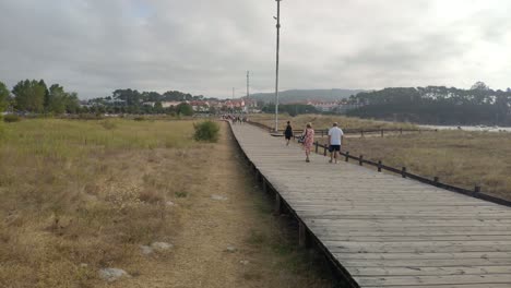 an elderly couple strolls over a wooden overpass near the beach on a cloudy gray morning, taking a panoramic view. porto-novo, galicia, spain