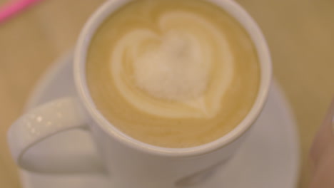 in a cup of coffee with foam girl pours sugar and stirs coffee with a spoon