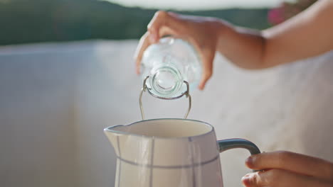 closeup woman hand pouring liquid in jug at summer balcony. lady holding bottle