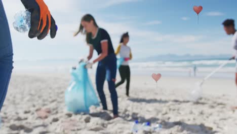 Animation-of-hearts-over-diverse-female-volunteers-picking-up-rubbish-on-beach