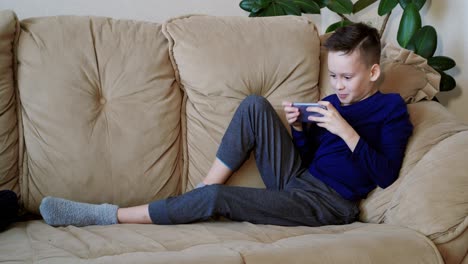 Child playing on smart phone. Relaxed boy playing on mobile phone on sofa in living room at home