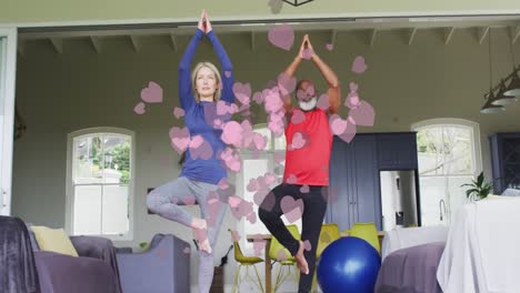 animation of heart icons over senior diverse couple practicing yoga at home
