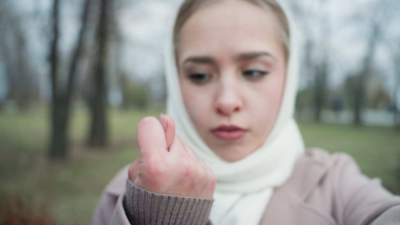 Young woman in scarf pleading with camera, emotional plea and determined gaze in frosty park, closeup hands reaching forward with raw vulnerability, winter trees and muted tones create cinematic mood