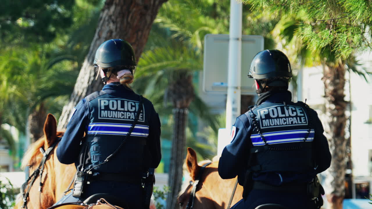 Nice, France - March 10, 2025: Two police women riding on horses on the street, near palm tres on a sunny day