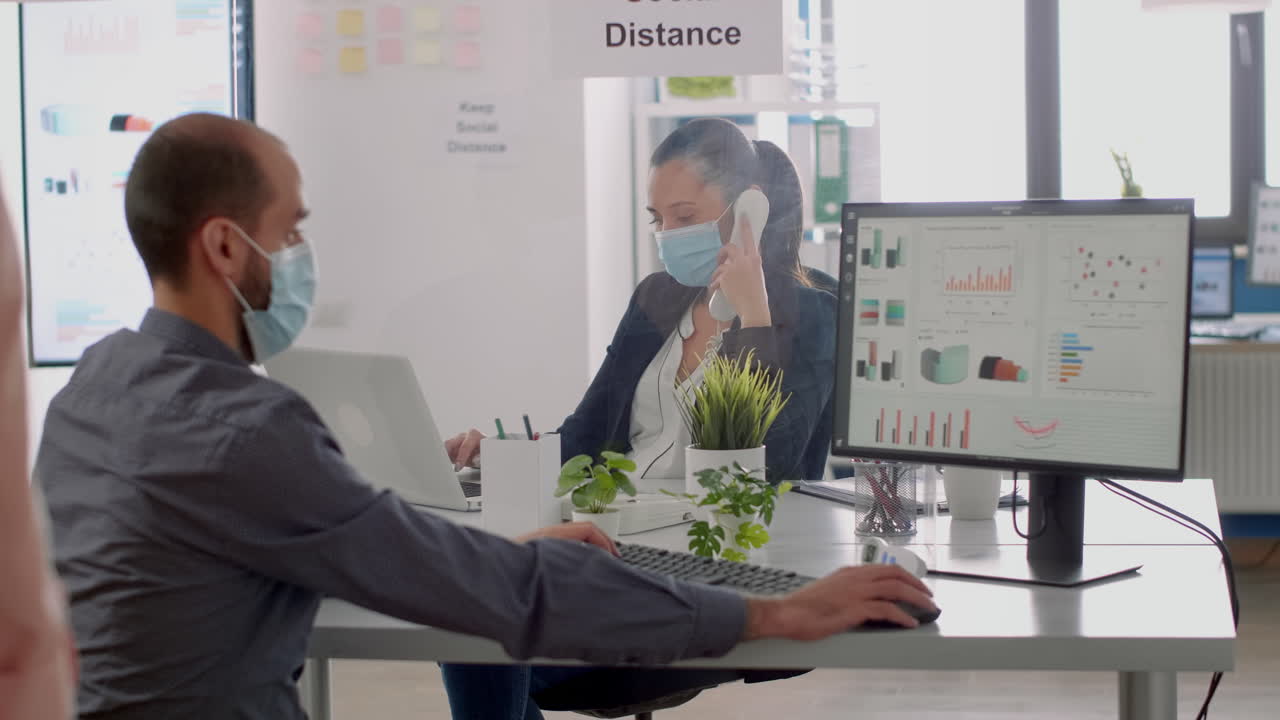 새로운 정상적인 회사 사무실에서 책상에 앉아 있는 얼굴 마스크를 착용한 동료들