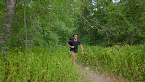 el excursionista masculino moderno en verano emerge del bosque y camina por el sendero hacia la cámara