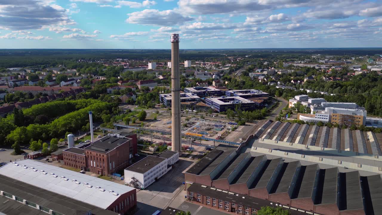 industrial buildings and a chimney in Hennigsdorf, Germany, with a train passing by. Perfect aerial view flight panorama orbit drone