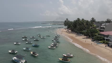 Niedrige-Überführung-Von-Festgemachten-Booten-Und-Schwimmern-Am-Sandstrand-Von-Sri-Lanka