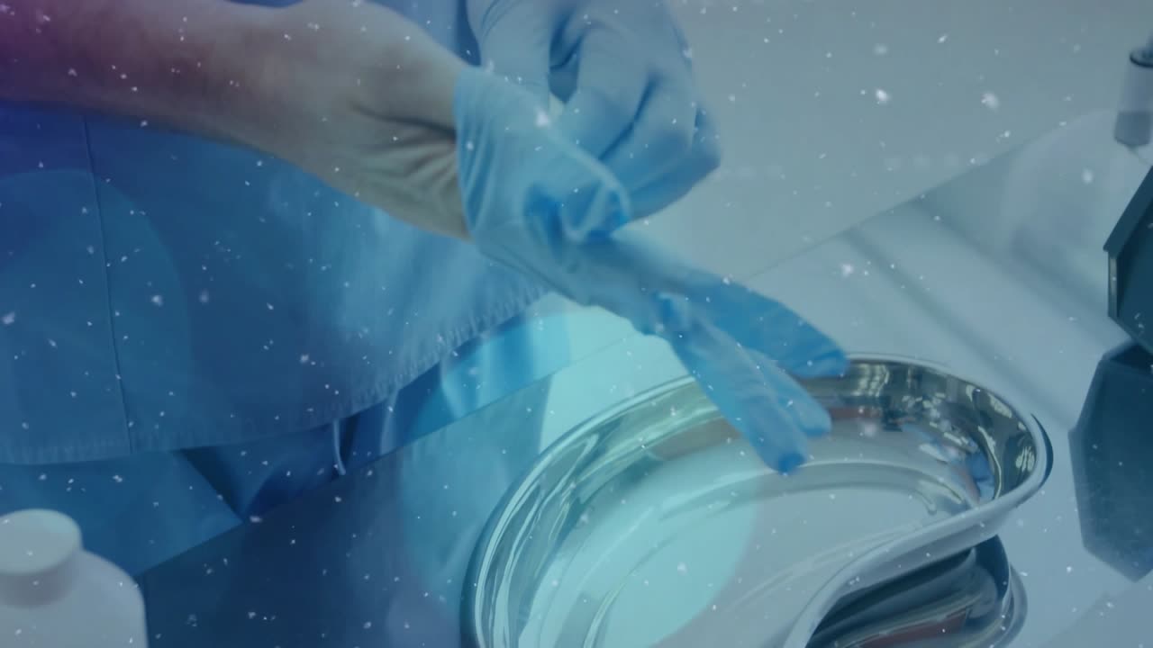 Clinician wearing blue scrubs at steel sink, reaching glove box, donning gloves for clinical task