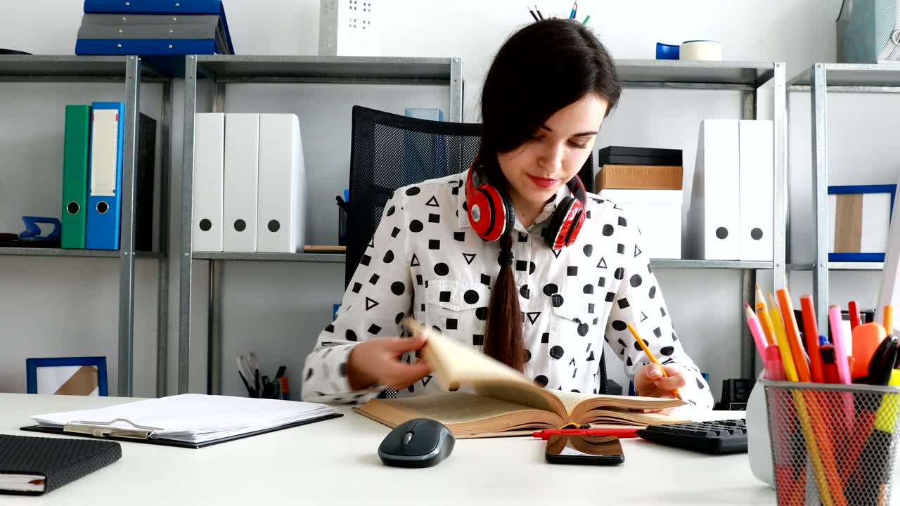 mujer con auriculares rojos en los hombros cerrando el libro y inclinándose hacia atrás