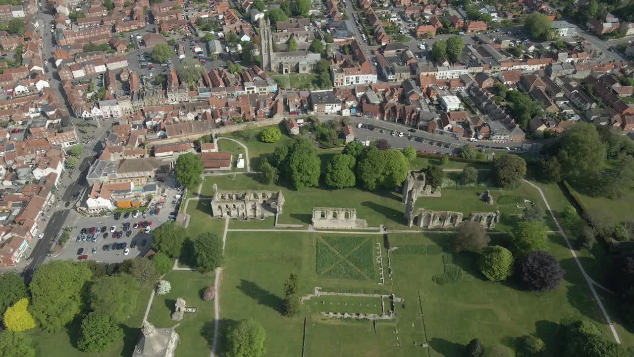 Aerial view of the Glastonbury Abbey ruins an 8th century monastery and gardens. Drone moving upwards over the ruins revealing the Glastonbury town in the background. 4K, 60fps.