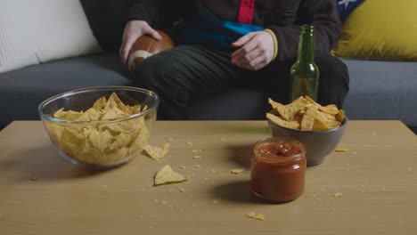 frustrated person at home watching american football game on tv with drinks snacks and ball