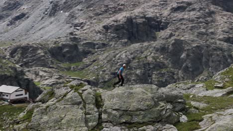 Man-walking-down-the-summit-of-a-top-rocky-mountain-during-hiking-adventure,-Italian-Alps