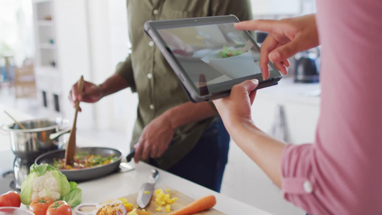 pareja afroamericana cocinando y usando tableta en la cocina