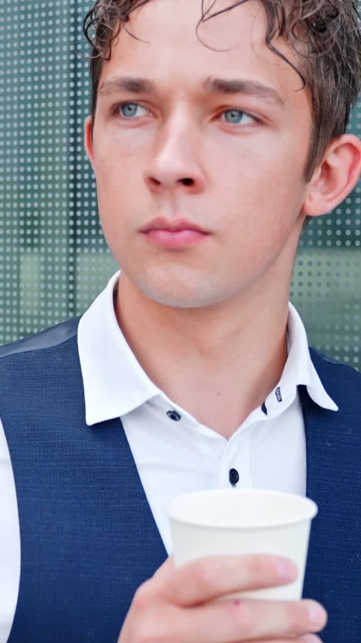 A vertical shot shows a young man in formal business attire leaning against a wall and drinking coffee. The camera tracks closer until it ends in a tight close-up of his face
