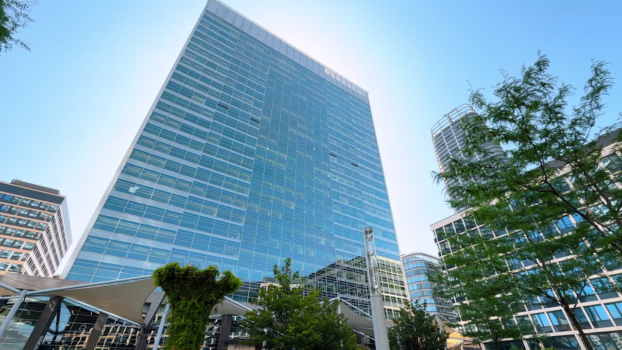 Green urban landscape scene. Tall glass buildings surround a vibrant green park with trees in the heart of a bustling city on a sunny day