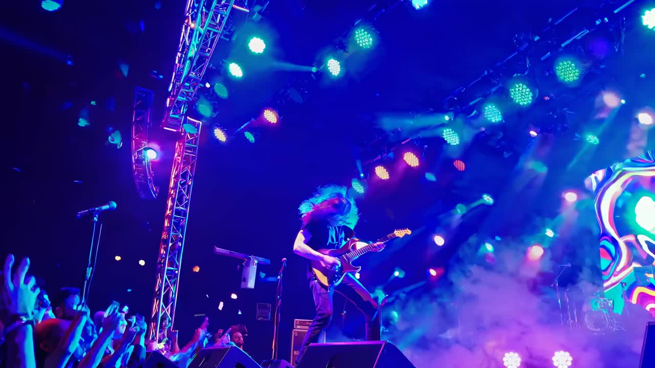 Scena video dinamica di un concerto con un’inquadratura dal basso che cattura un chitarrista sul palco, luci vivaci