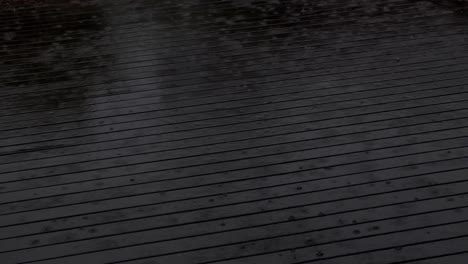 raindrops splashing on dark wooden deck during a heavy downpour