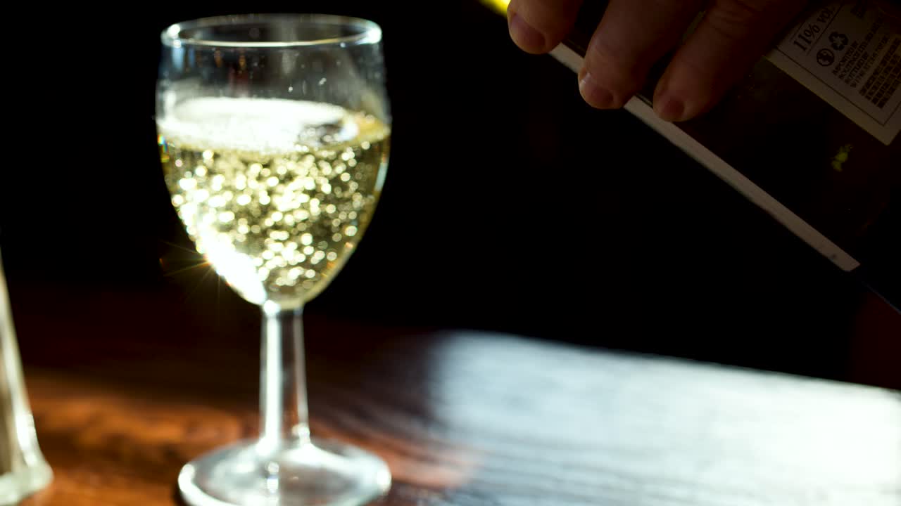 Sparkling drink poured into clear wine glass, backlit, with bubbles rising in warm indoor setting