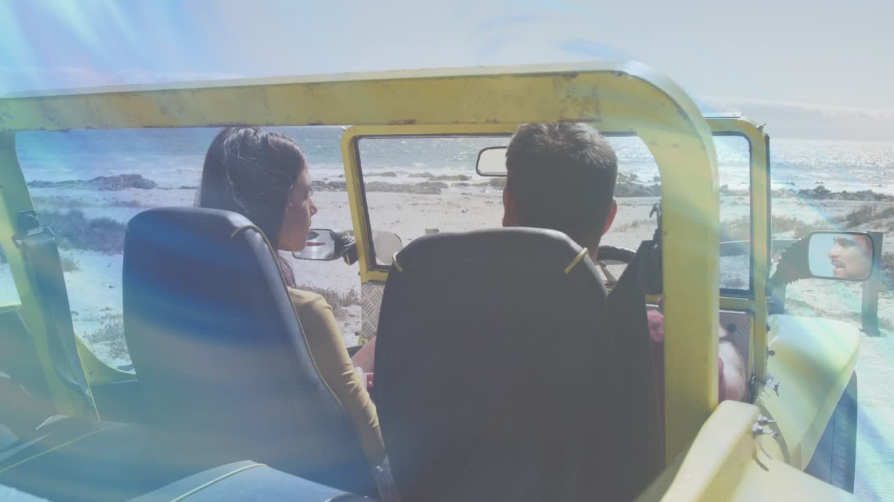 Female passenger turning to male driver, driver gesturing toward ocean in yellow Jeep sharing view