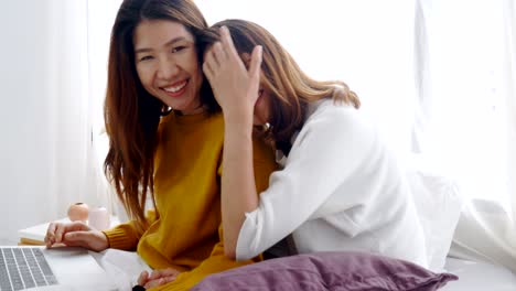 젊은 아시아 레즈비언 커플이 집에서 침실에서 노트북을 사용하고 있습니다.