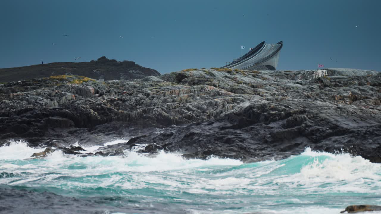 Dramatic view of the Atlantic Ocean waves crashing against the rocky coast of Norway, with a bridge in the background