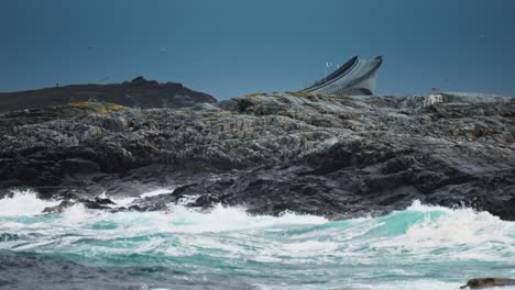 dramatic view of the atlantic ocean waves crashing against the rocky coast of norway, with a bridge in the background