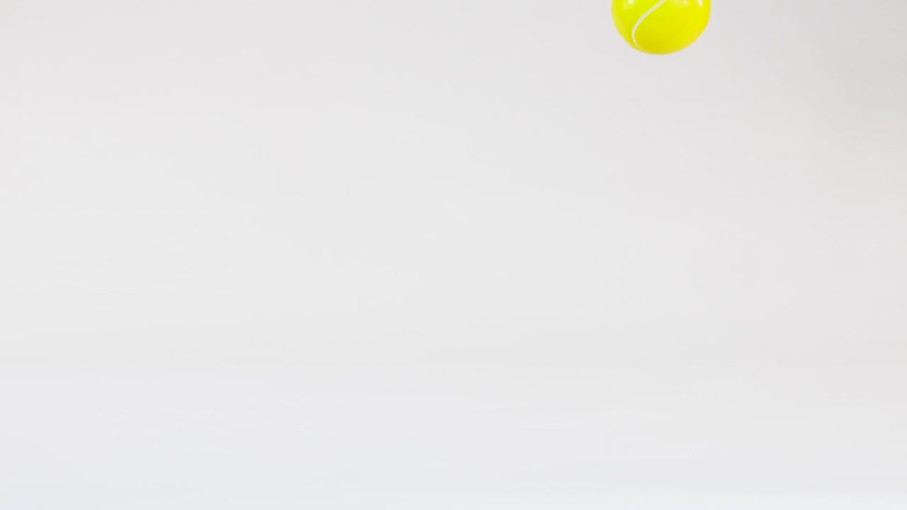 A single yellow tennis ball bounces across a bright white studio background with soft lighting
