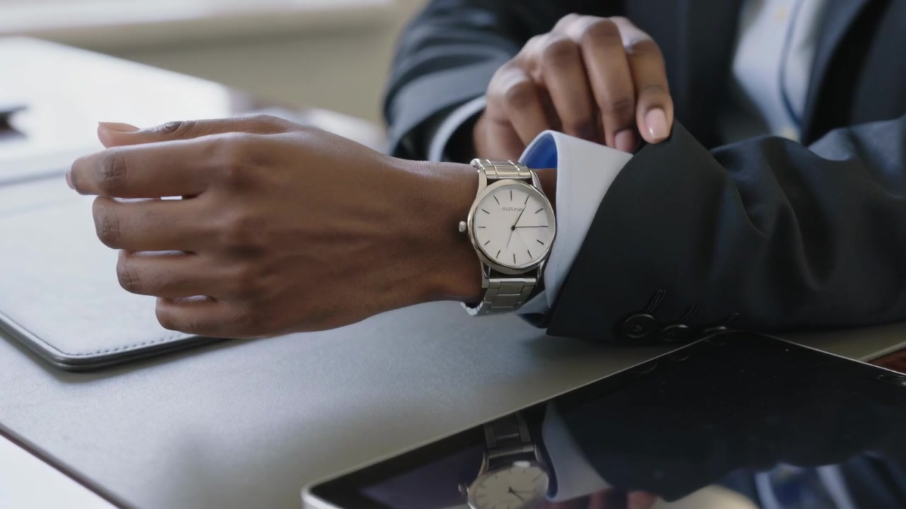 Adjusting man in dark suit pulling cuff after rest at desk with leather pad, checking watch