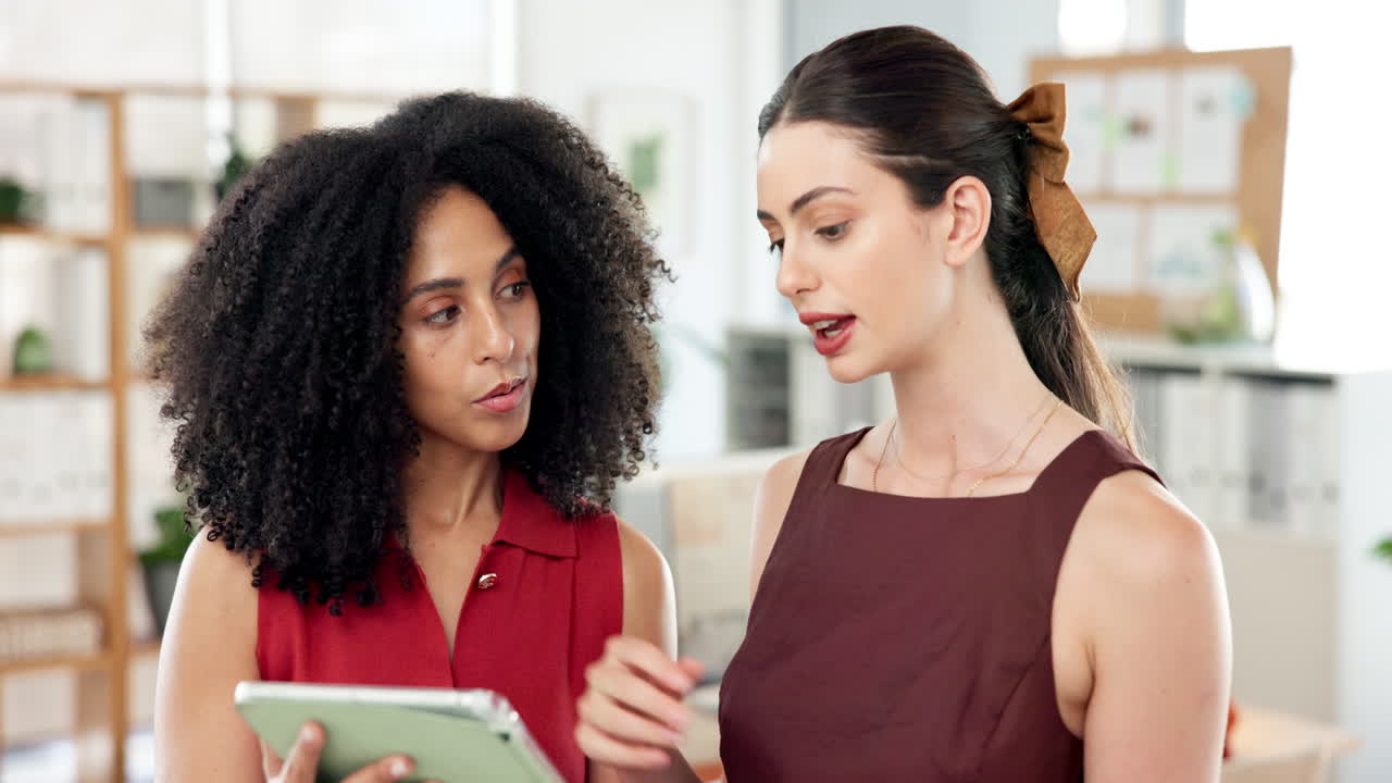 Dos mujeres profesionales discutiendo negocios en una tableta digital en una oficina
