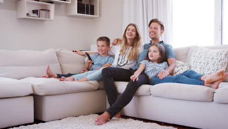 Family-Sitting-On-Sofa-At-Home-Watching-TV-Together