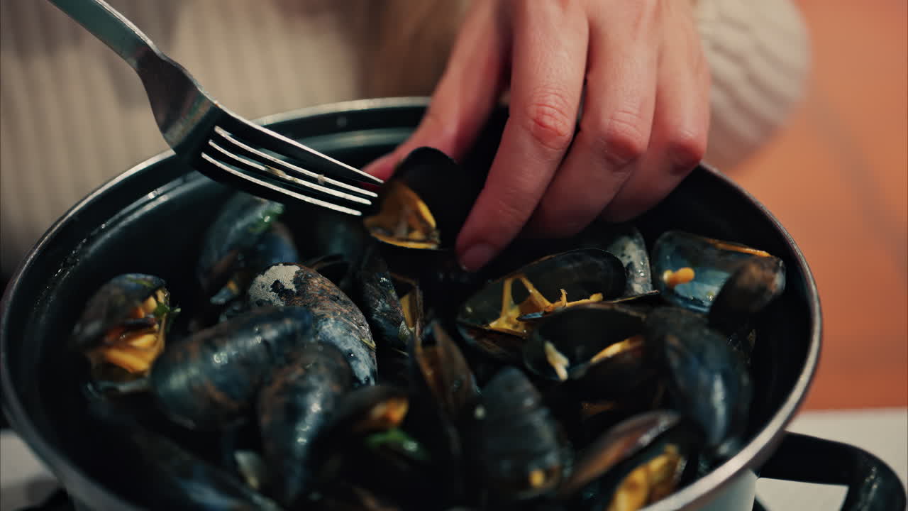 Close up of a woman eating mussels from a pan with a fork