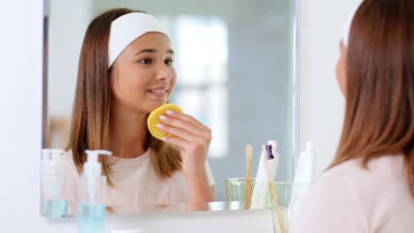 Belleza,-Higiene-Y-Concepto-De-Personas-Adolescente-Con-Esponja-Limpiadora-Limpiando-La-Piel-Del-Rostro-Y-Mirándose-En-El-Espejo-Del-Baño