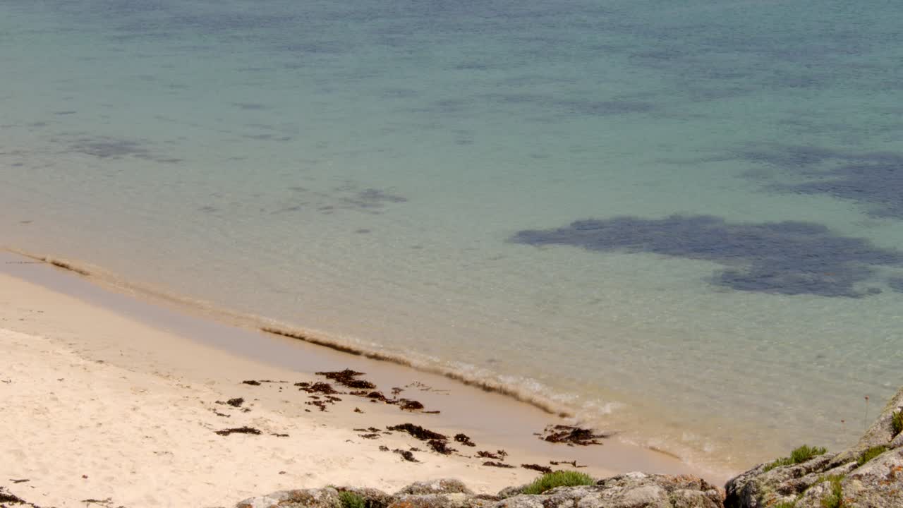 looking down onto the beach with the sea lapping on to the sand on St Agnes and Gugh at the Isles of Scilly