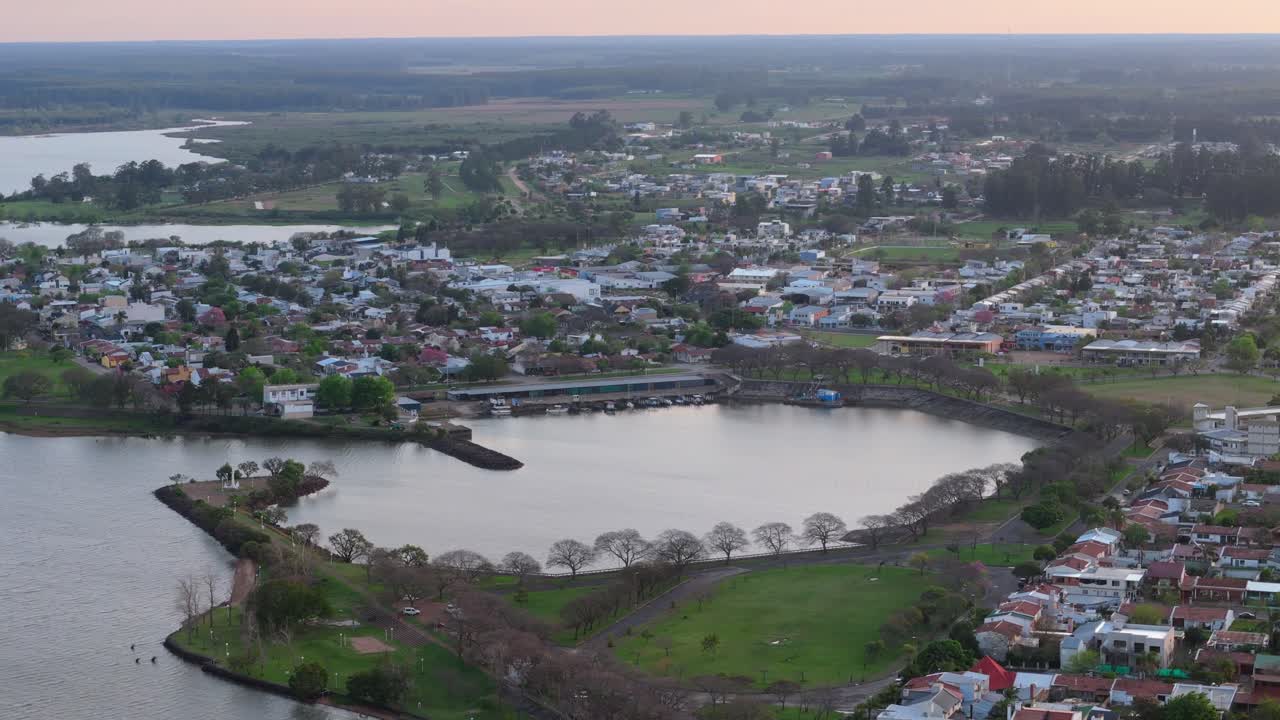 Aerial shot of a town beside a waterbody at sunset, showcasing houses, roads, and greenery, with a serene and picturesque atmosphere in Federacion, Entre Ríos, Argentina