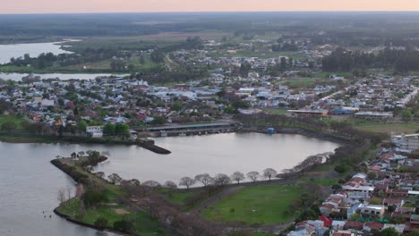 aerial shot of a town beside a waterbody at sunset, showcasing houses, roads, and greenery, with a serene and picturesque atmosphere in federacion, entre ríos, argentina