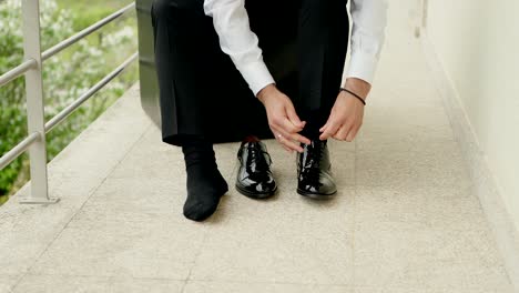 man ties one shoe while wearing one sock during wedding prep moment