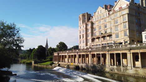 Pulteney-Weir-Y-El-Empire-Hotel-En-Bath,-Somerset-En-Una-Hermosa-Mañana-De-Verano-Que-Se-Desvanece-En-Diagonal-Hacia-El-Cielo-Azul-Claro-Con-Una-Gaviota-Volando-A-Través-Del-Marco-En-Cámara-Lenta