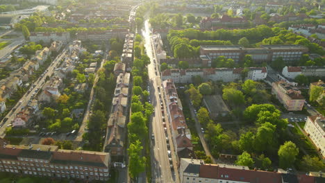 dzielnica mieszkaniowa gdańsk latem o złotej godzinie, pojazdy zaparkowane na poboczu drogi wraz z budynkami, bloki domów z zielonymi parkami - widok z lotu ptaka, ruch w tył