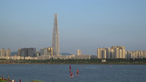 Windsurfer,-Die-Zur-Goldenen-Stunde-Auf-Dem-Han-Fluss-Neben-Der-Jamsil-Brücke-Und-Dem-Lotte-World-Tower-Surfen---Statische-Weitwinkelaufnahme