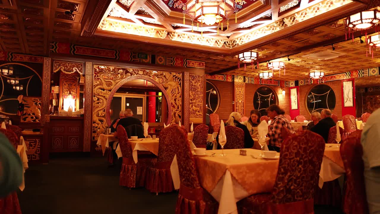 Warmly lit Chinese restaurant interior with diners seated, browsing menus, and conversing at tables