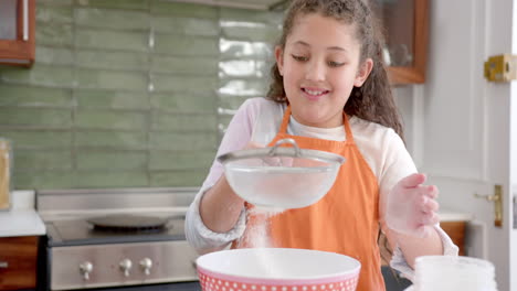feliz chica biracial con el cabello largo y rizado tamizando harina y sonriendo en la cocina soleada