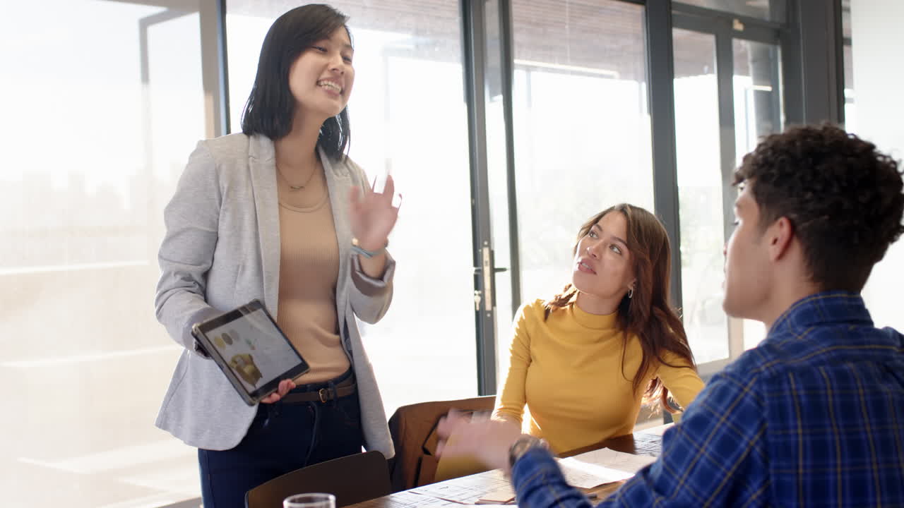 Design ideas, woman holding tablet while multiracial colleagues listen attentively, at office