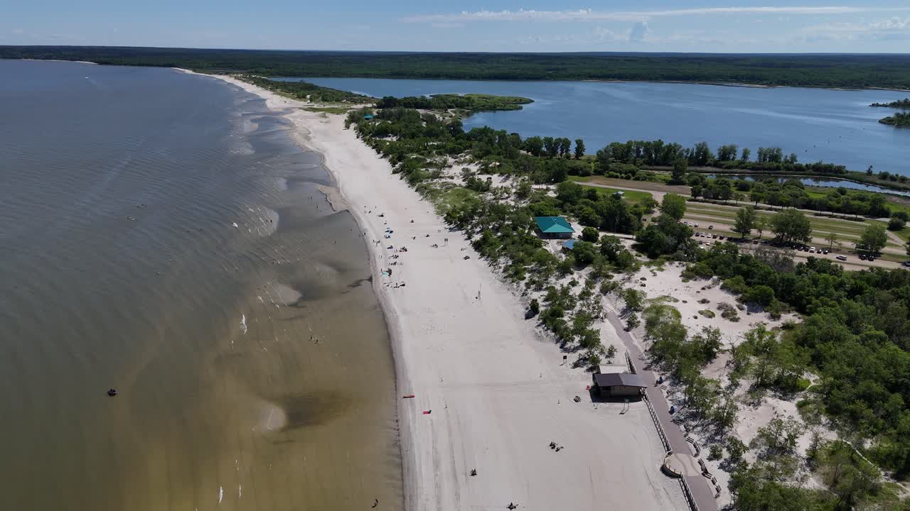 Riprese aeree con drone da lontano sul Lago Winnipeg che guarda a nord a Grand Beach, Manitoba. Giornata estiva con persone sulla spiaggia, costa sabbiosa, laguna e foresta boreale sullo sfondo.