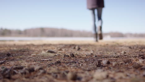 Woman-in-boots-and-jeans-strolls-in-outdoors-on-lake-edge,-low-shallow-focus